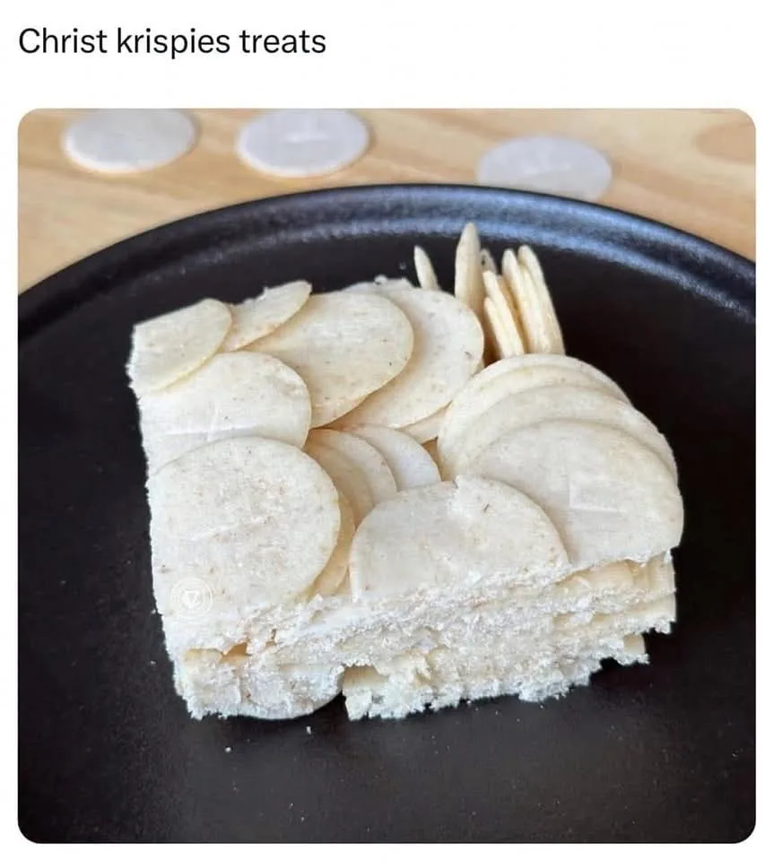 A square slice of a light-colored, layered dessert sits on a black plate, decorated with thin, round, pale crackers arranged…