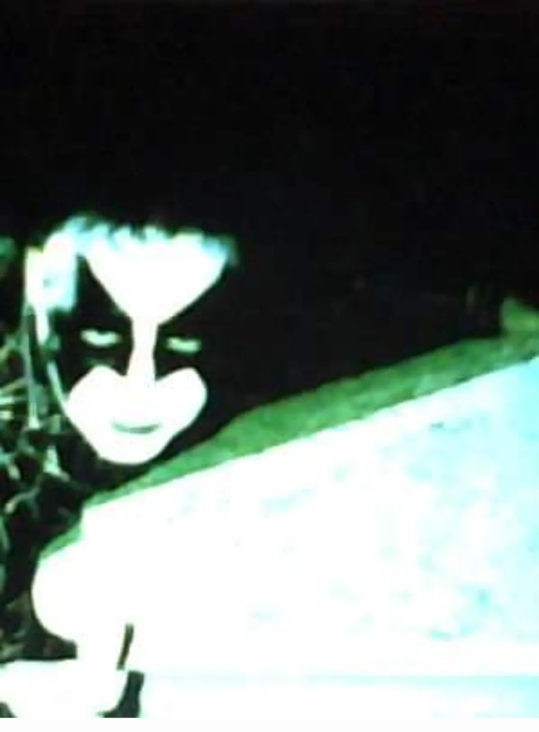 A low-resolution, grainy image shows a person with stark black and white face paint resembling a horror or goth makeup…