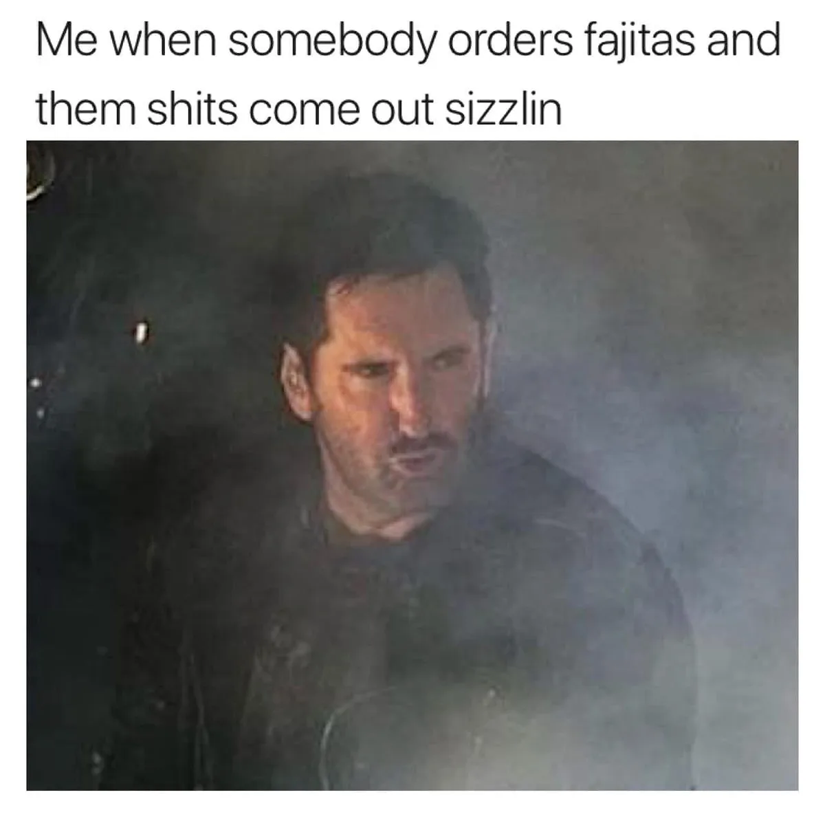 A grainy, smoky image of a man with a serious, intense expression, overlaid with the text 'Me when somebody orders fajitas…