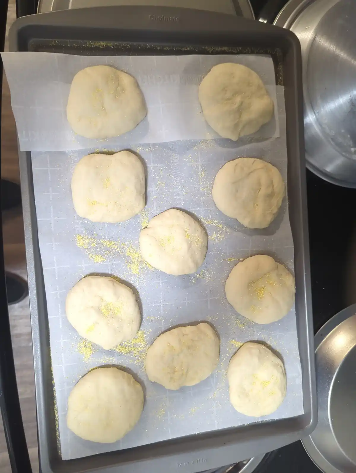 A baking sheet lined with parchment paper holds nine uncooked, roughly shaped dough balls dusted with yellow seasoning. The…
