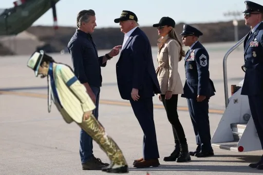 A man in a military-style uniform is bent over, appearing to be in a deep bow or salute, while standing near a group of…