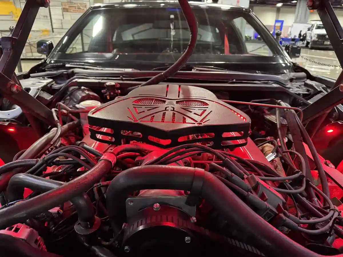 A close-up shot of a car's engine bay with a custom black air intake cover shaped and illuminated like Darth Vader's helmet…
