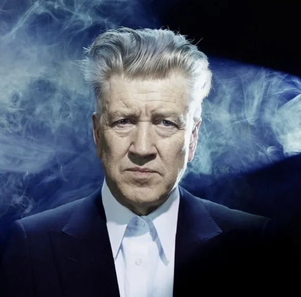 a close-up portrait of a man with gray hair, wearing a dark suit and white shirt, set against a dark background with…