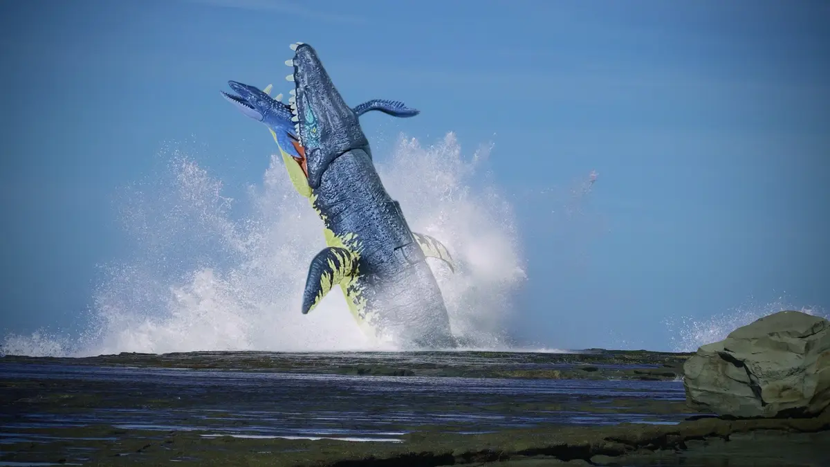 A large, blue and yellow plastic toy dinosaur, resembling a crocodylomorph, is dramatically leaping out of shallow water…