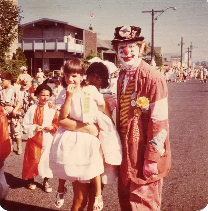 A vintage photo shows a man in a full clown costume with a red nose and white face paint standing next to two young girls in…
