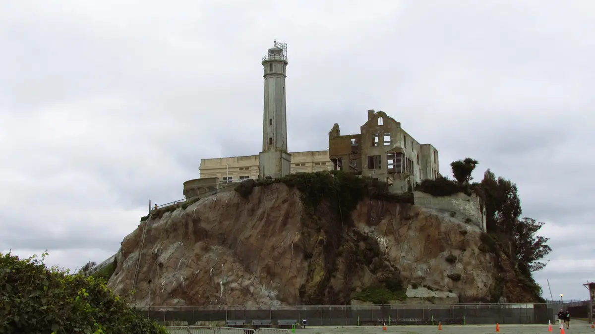 The image shows the ruins of Alcatraz Island prison in San Francisco, featuring a lighthouse and crumbling concrete…