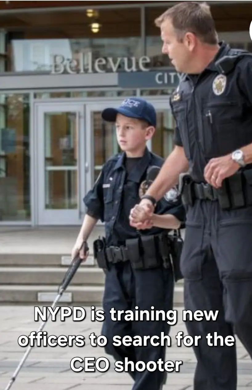 A police officer holds the hand of a young boy dressed in a police uniform, complete with a cap, vest, and a long cane. They…