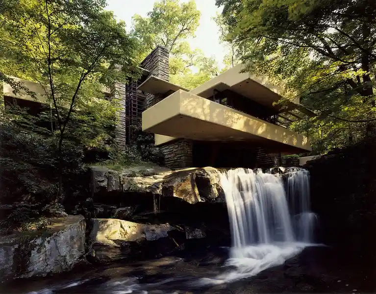 a photograph of a modernist house with cantilevered concrete balconies and stone walls, nestled among lush green trees, with…