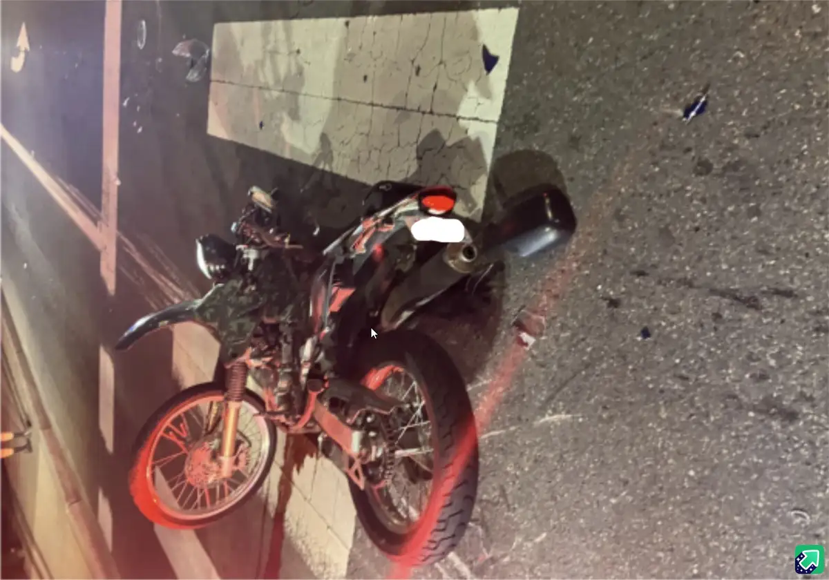 A motorcycle lies on its side on a cracked asphalt road at night, next to a faded white painted line, with scattered debris…