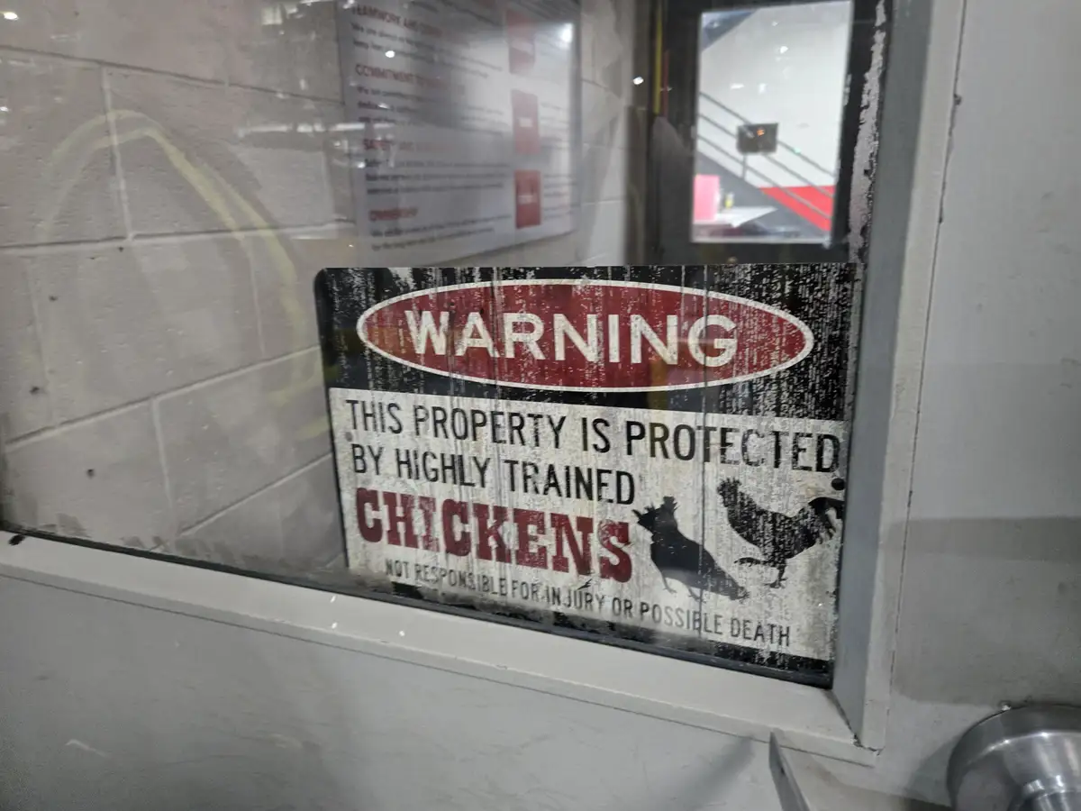 A weathered warning sign is taped to a glass door, stating that the property is protected by 'highly trained chickens' and…