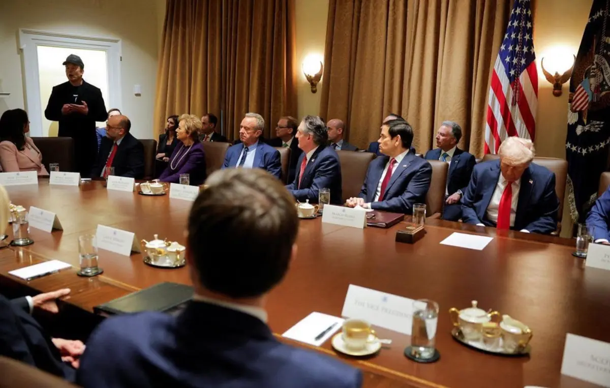 a photo of a formal meeting with several officials seated around a large wooden table, including Donald Trump at the right…