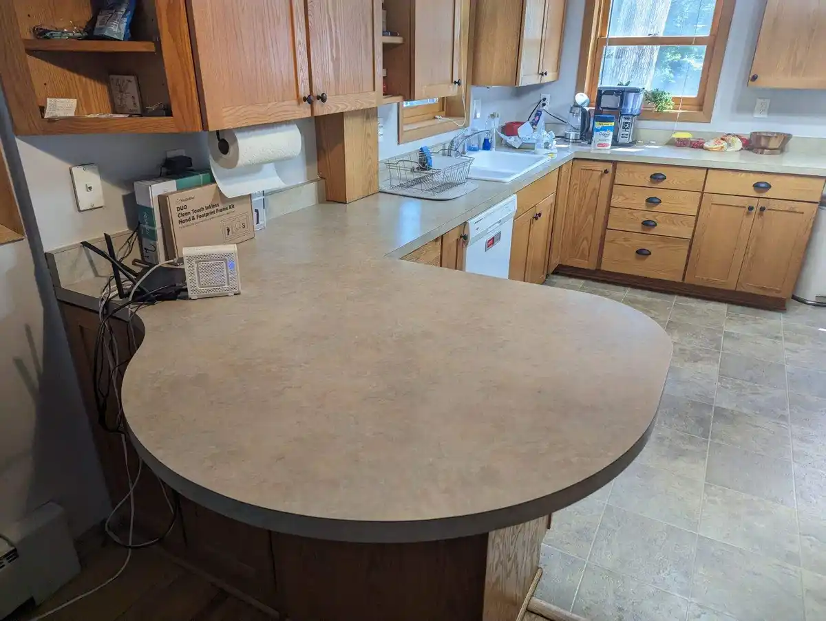A photo of a clean, empty kitchen island with wooden cabinets and tiled floors, featuring a box labeled 'DUO Clean Touch…