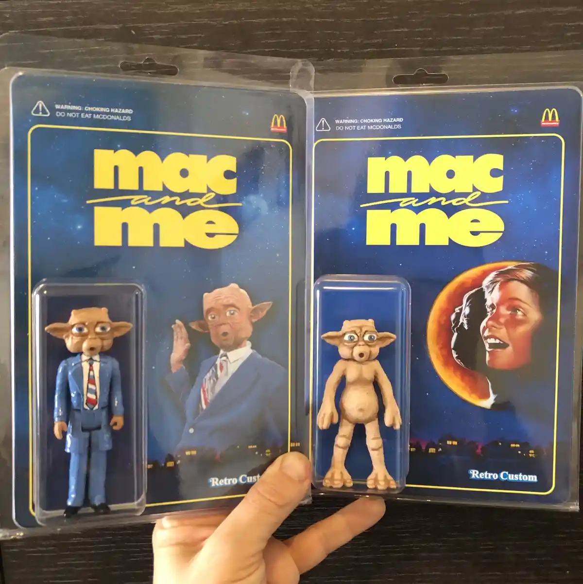 Two McDonald's 'Mac and Me' action figure packages are held side-by-side, each featuring a different version of the alien…
