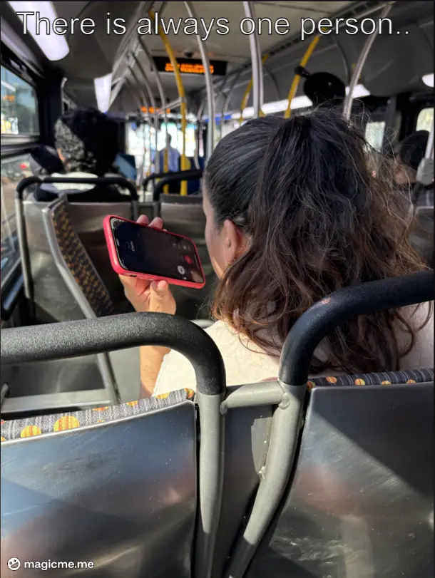 A person with dark hair in a ponytail sits on a public bus, holding a red phone with the screen facing them, seemingly…