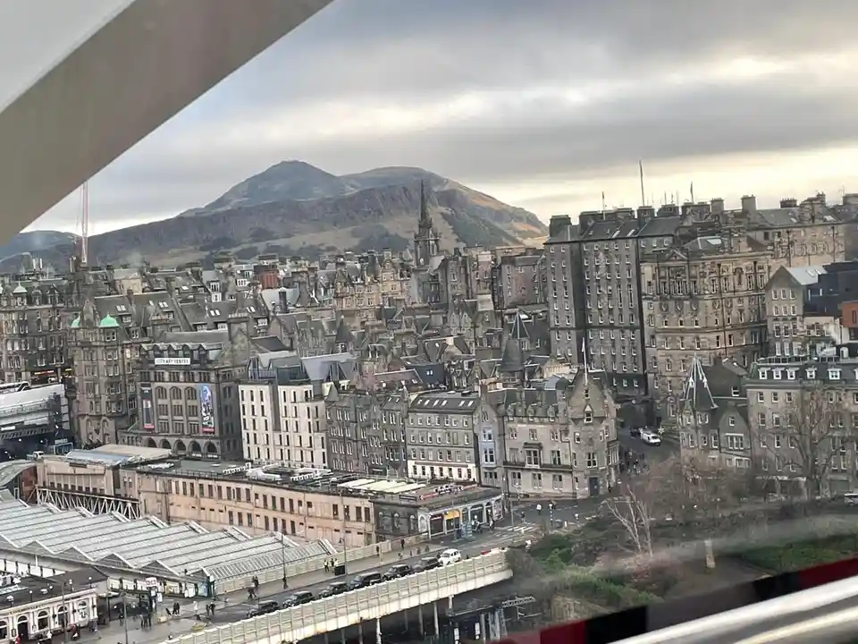 A high-angle photograph shows a dense urban landscape of Edinburgh, Scotland, with historic stone buildings and a prominent…