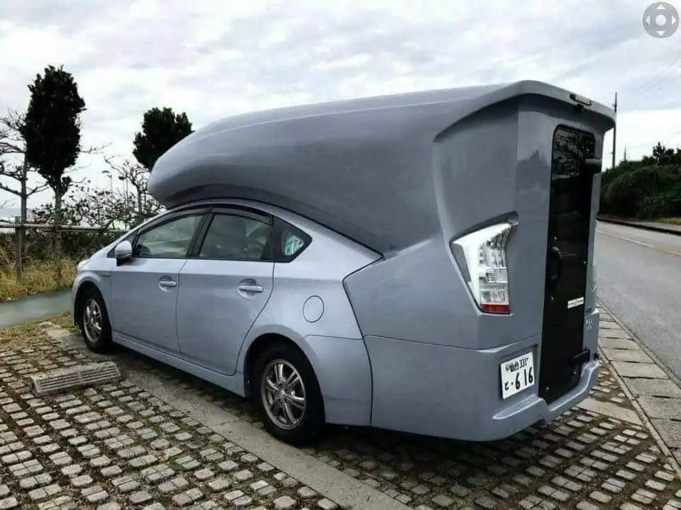 A silver Toyota Prius is parked on a cobblestone surface with a large, smooth, gray, curved dome-shaped roof extension that…
