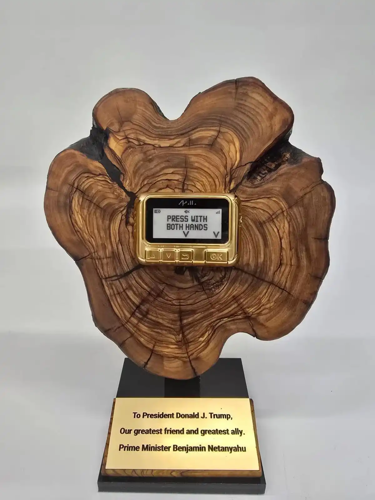 A golden, old-style phone is embedded in a large, ornate wooden base resembling a tree stump, mounted on a black stand with…