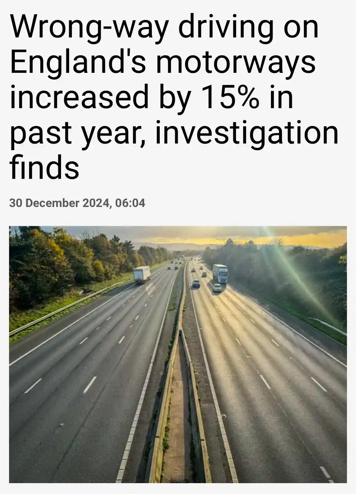 The image displays a wide, multi-lane motorway with cars and trucks traveling in both directions under a bright sky with sun…