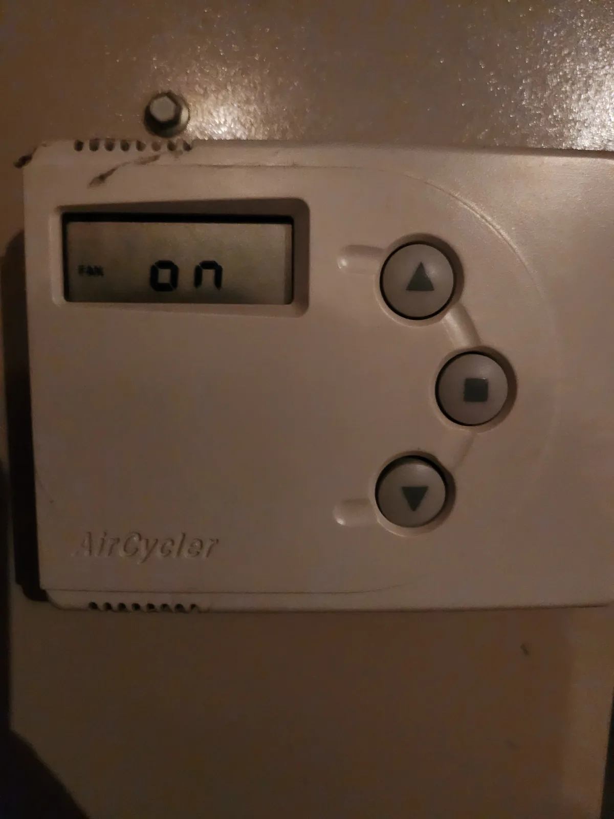 A close-up of a beige 'AirCycler' thermostat mounted on a textured wall, showing a digital display that reads 'FAN ON' with…
