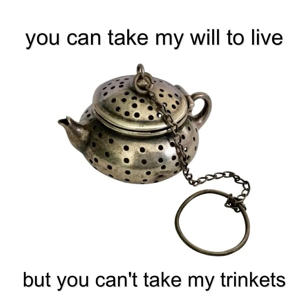A vintage-style metal tea infuser shaped like a small teapot with a chain and ring, set against a plain white background…