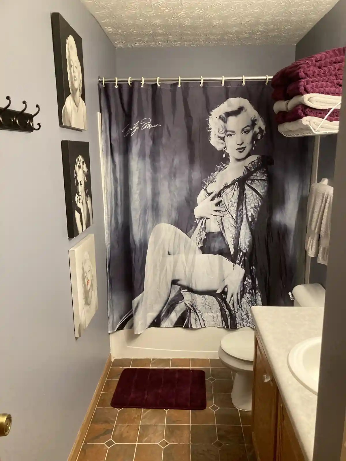 A bathroom features a shower curtain with a large black-and-white photo of Marilyn Monroe, her signature visible, and three…