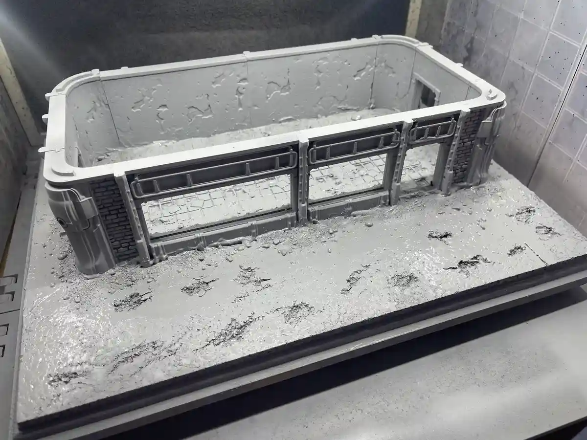 A 3d printed diorama model, resembling a ruined building or bridge structure, is shown covered in a thick, wet, gray…