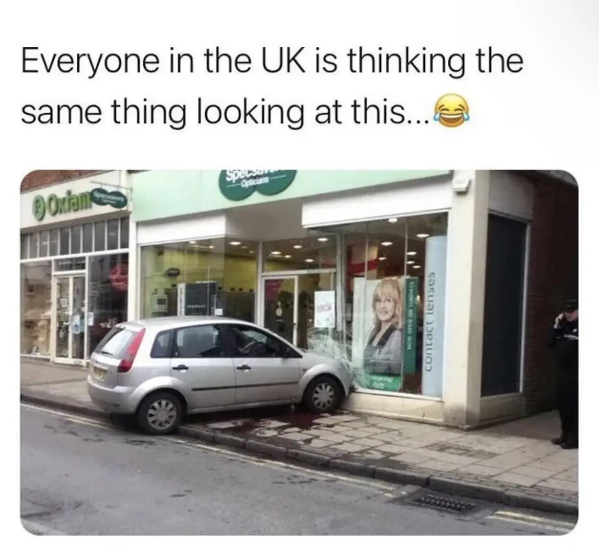 A silver car is parked on the street and has collided with the front window of a Specsavers optician shop, shattering the…