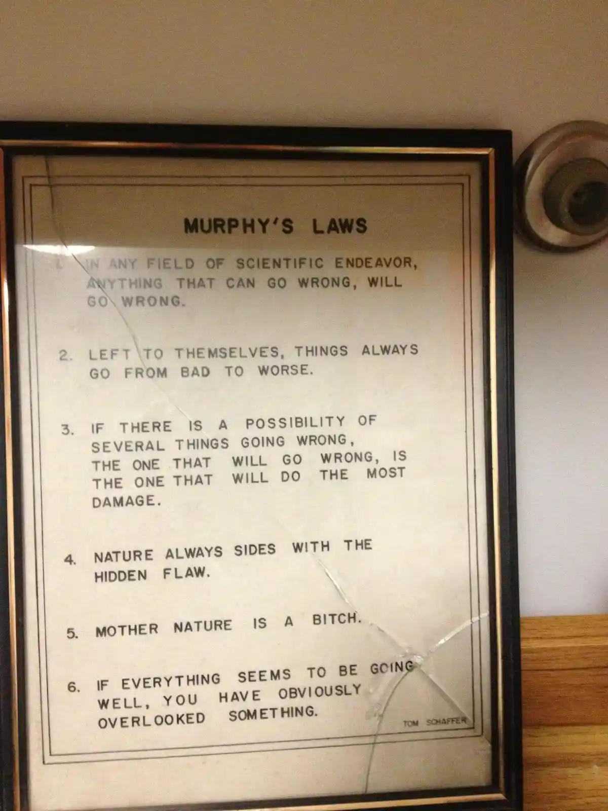 A framed poster titled 'MURPHY'S LAWS' lists six pessimistic rules about inevitable failure, mounted on a wall next to a…