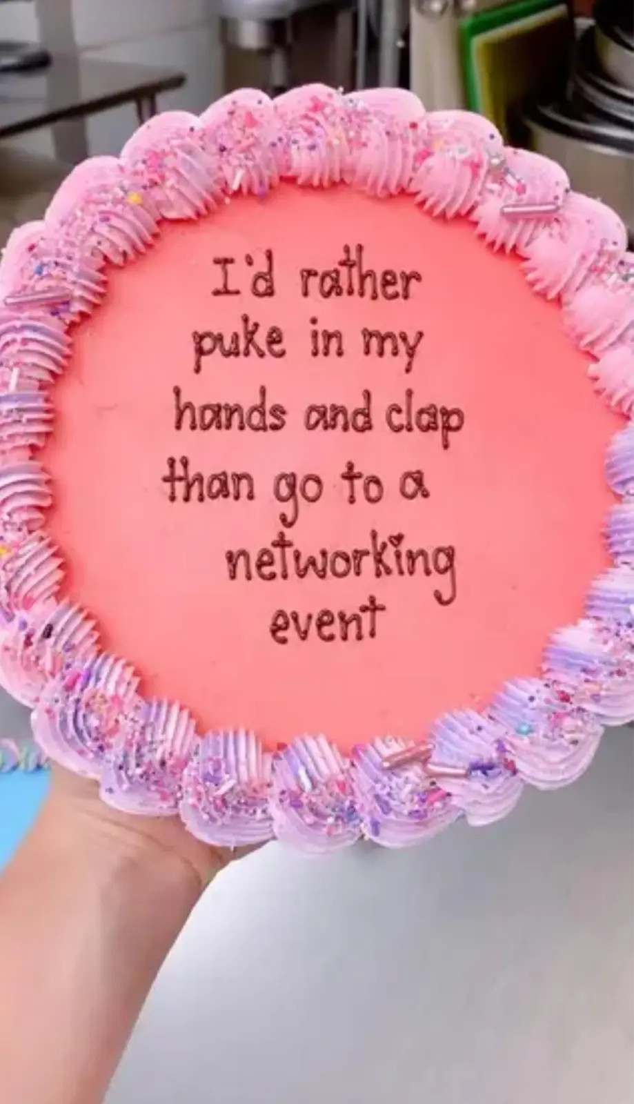 A hand holds a round cake with pink and purple frosting and sprinkles, featuring the text 'I'd rather puke in my hands and…