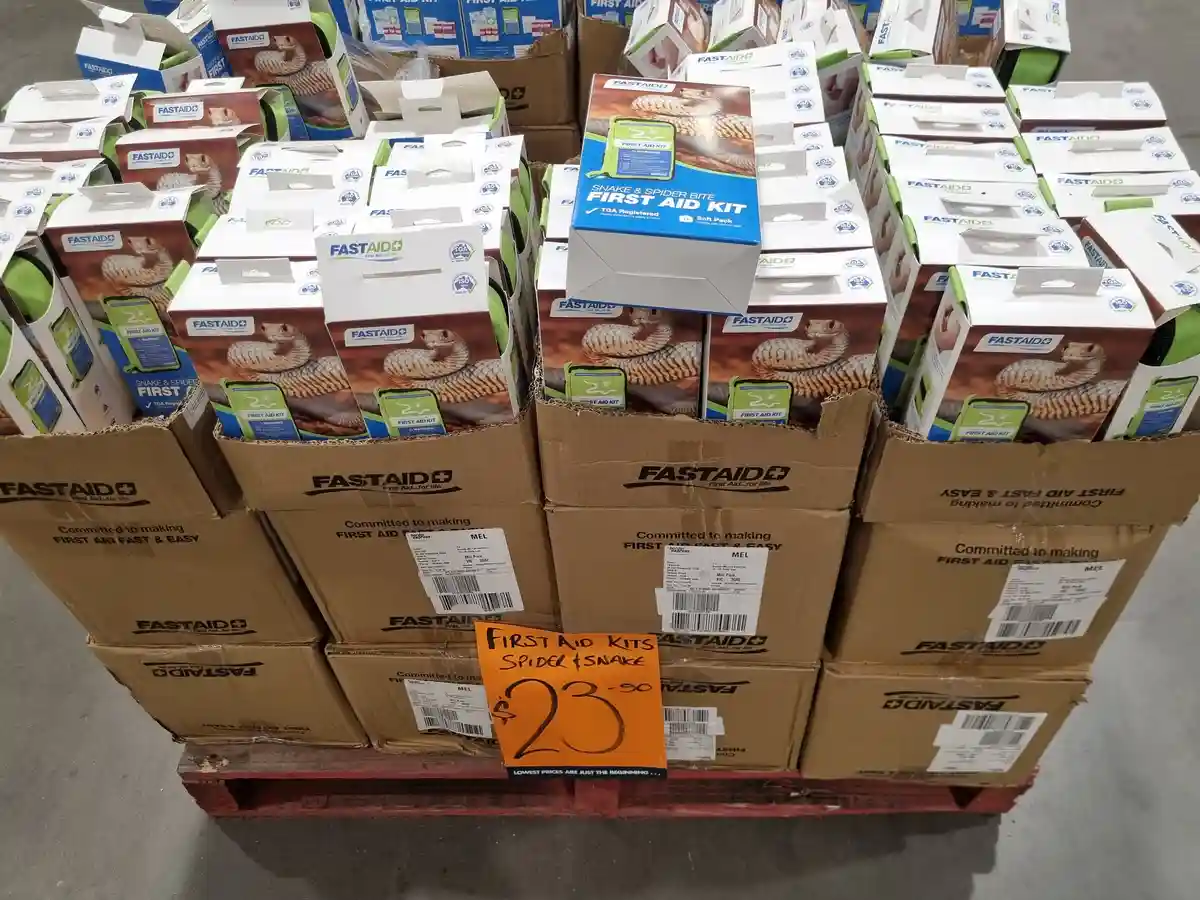 A pallet stacked with cardboard boxes of 'FASTAID' brand 'Snake & Spider Bite First Aid Kits', each box featuring an image…