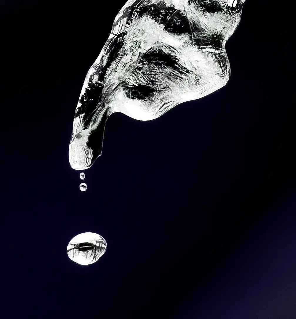 A high-contrast black-and-white image shows a large, textured ice finger pointing downward, with three droplets falling from…