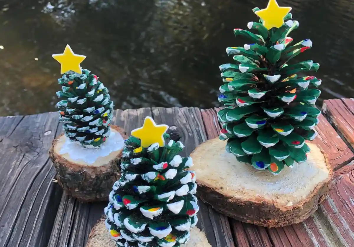 Three handcrafted Christmas trees made from painted pinecones, each topped with a yellow star and mounted on wooden tree…