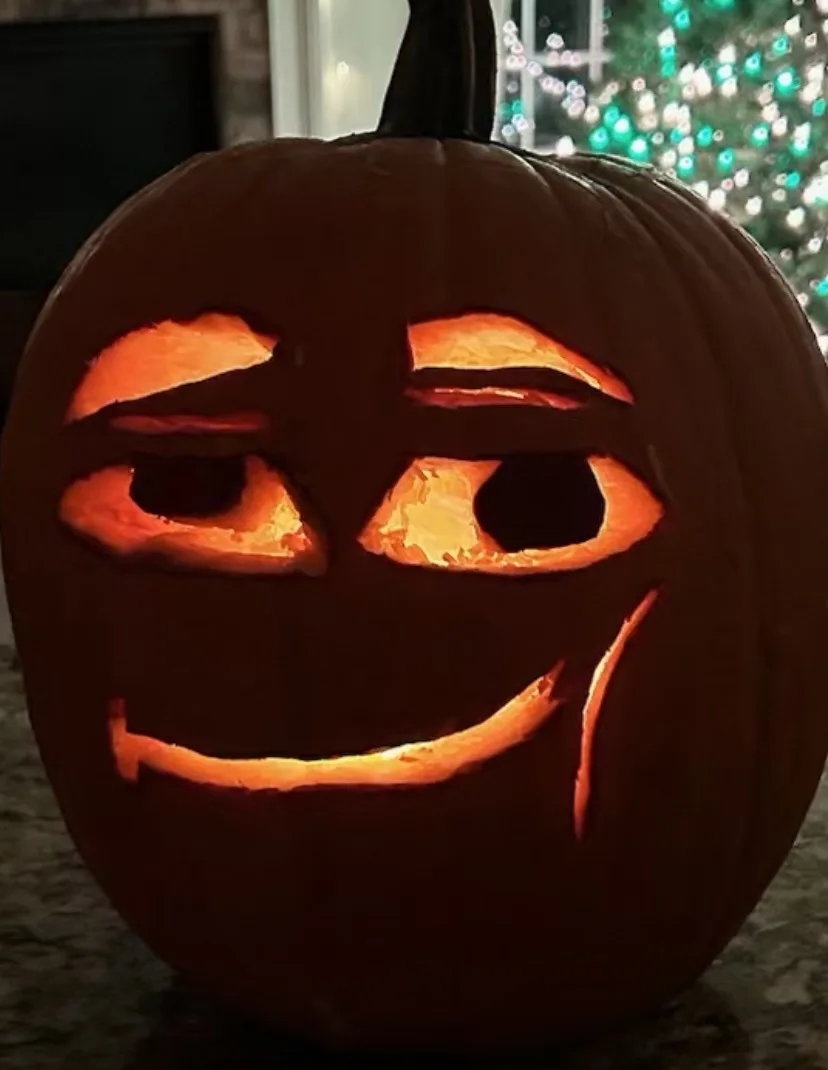 A carved pumpkin with a glowing orange interior, featuring the iconic 'eyebrows up, one eye closed, smiling, tear drop'…