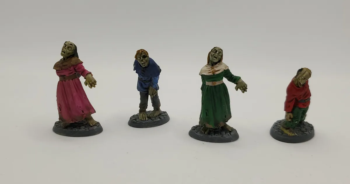 Four painted miniature zombie figures in medieval-style clothing stand in a row on a plain white background. Each figure has…