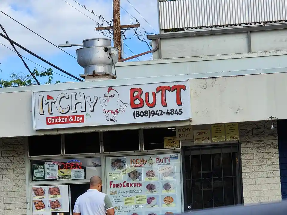A storefront with a large sign reading 'Itchy Butt Chicken & Joy' featuring a cartoon chicken in sunglasses and shorts. The…