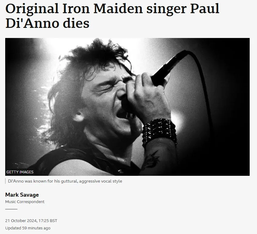 A black and white photo shows Paul Di'Anno, original Iron Maiden singer, singing aggressively into a microphone with his…