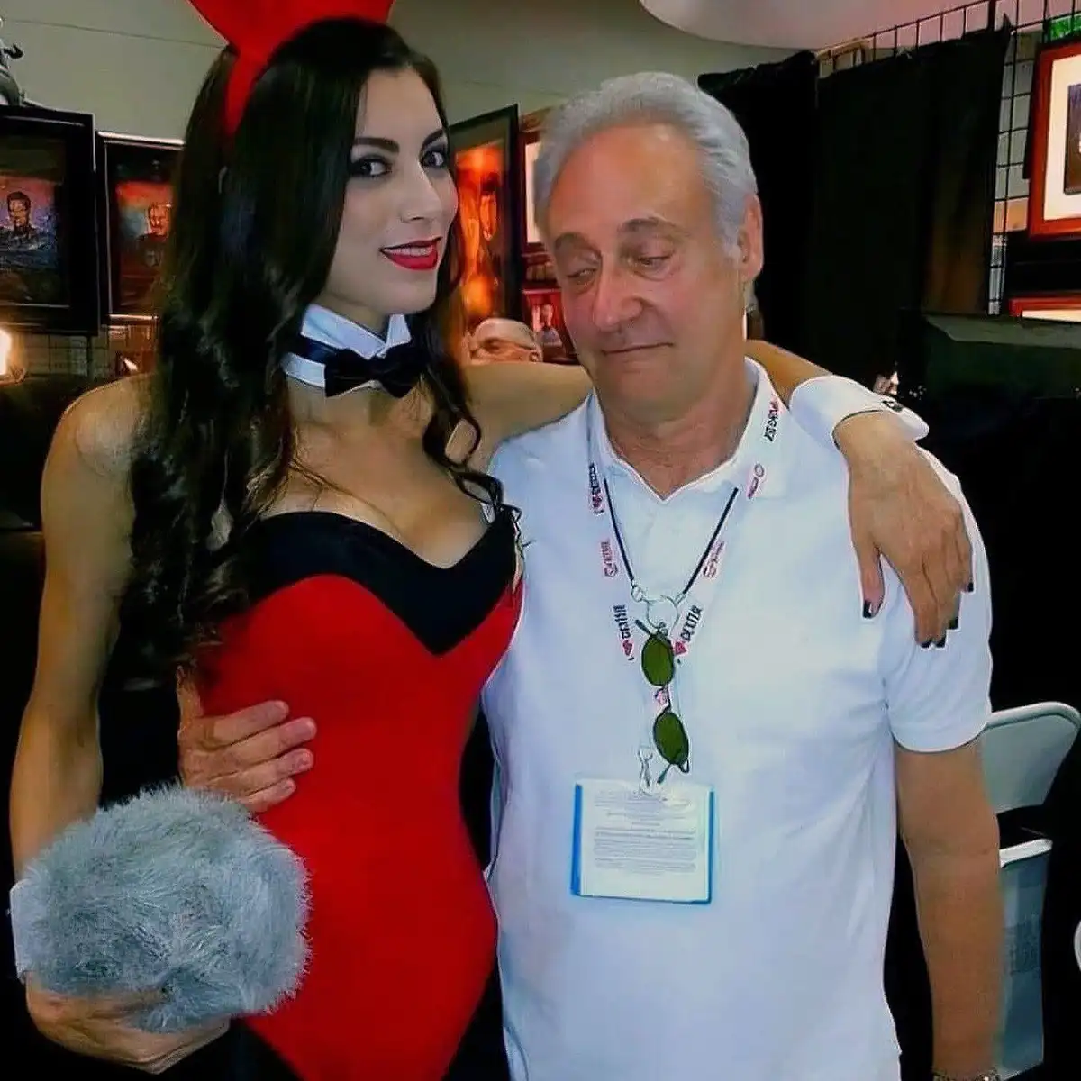 A woman in a red and black Catwoman costume with a bow tie and grey furry glove poses with an older man in a white polo…