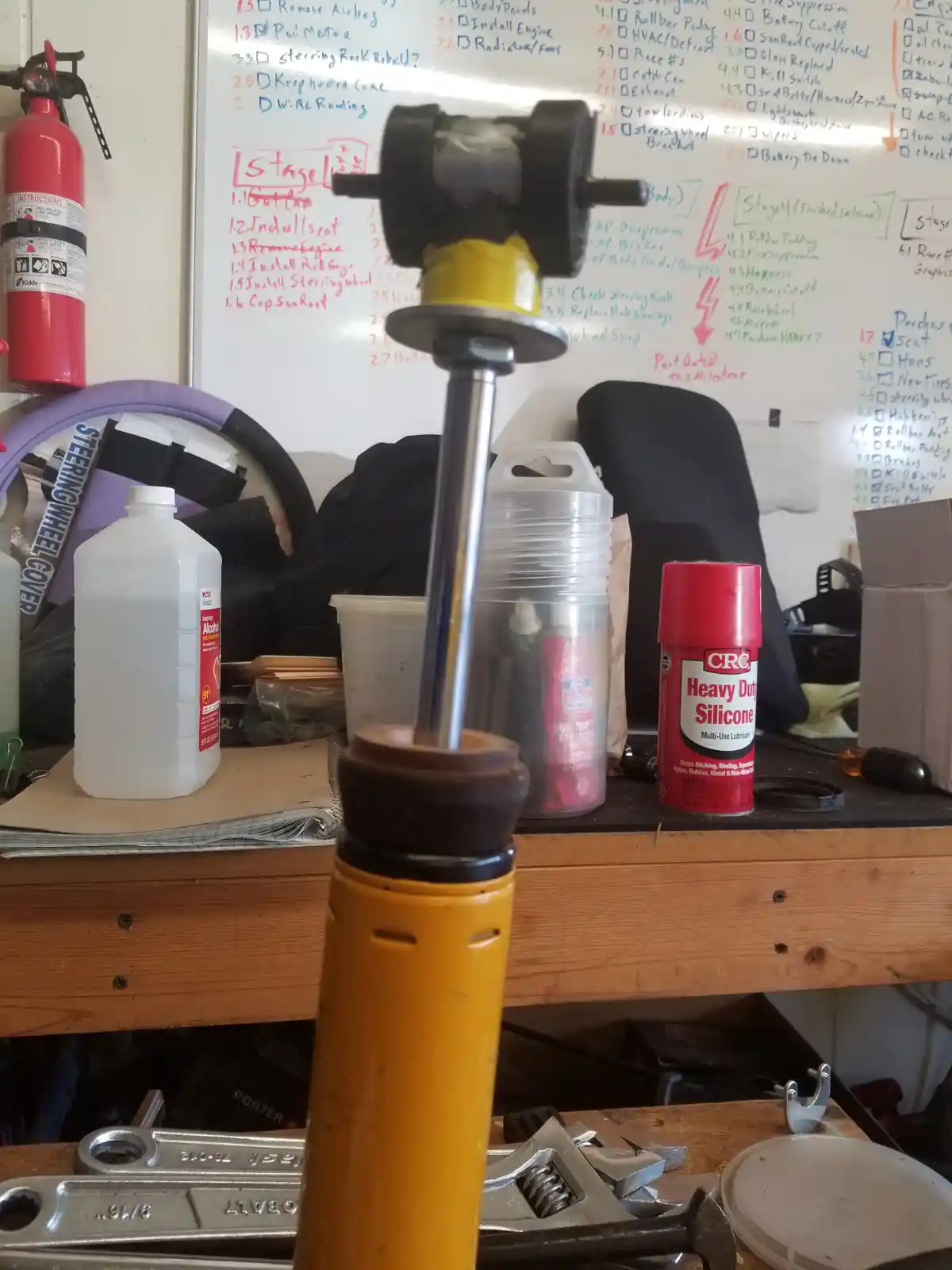 A close-up photo shows a yellow and black steering column assembly standing upright on a cluttered wooden workbench in a…