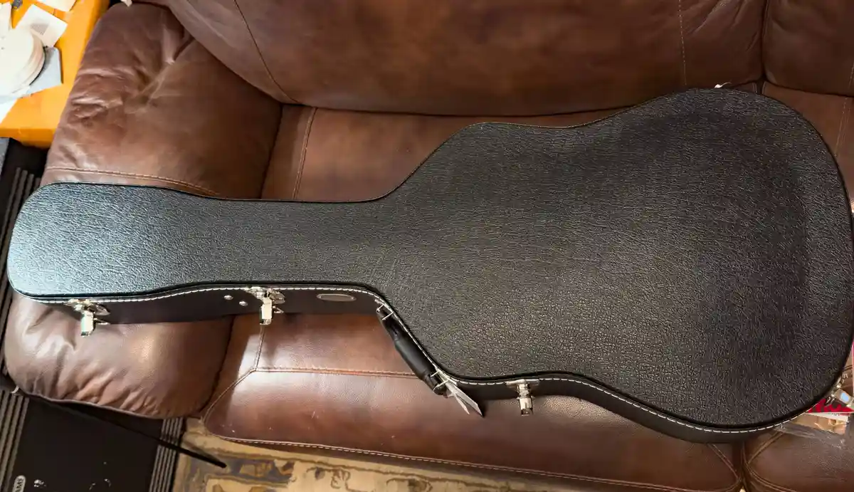 A black, textured guitar case with silver latches is lying open on a brown leather couch. The overlaid text reads 'i bought…