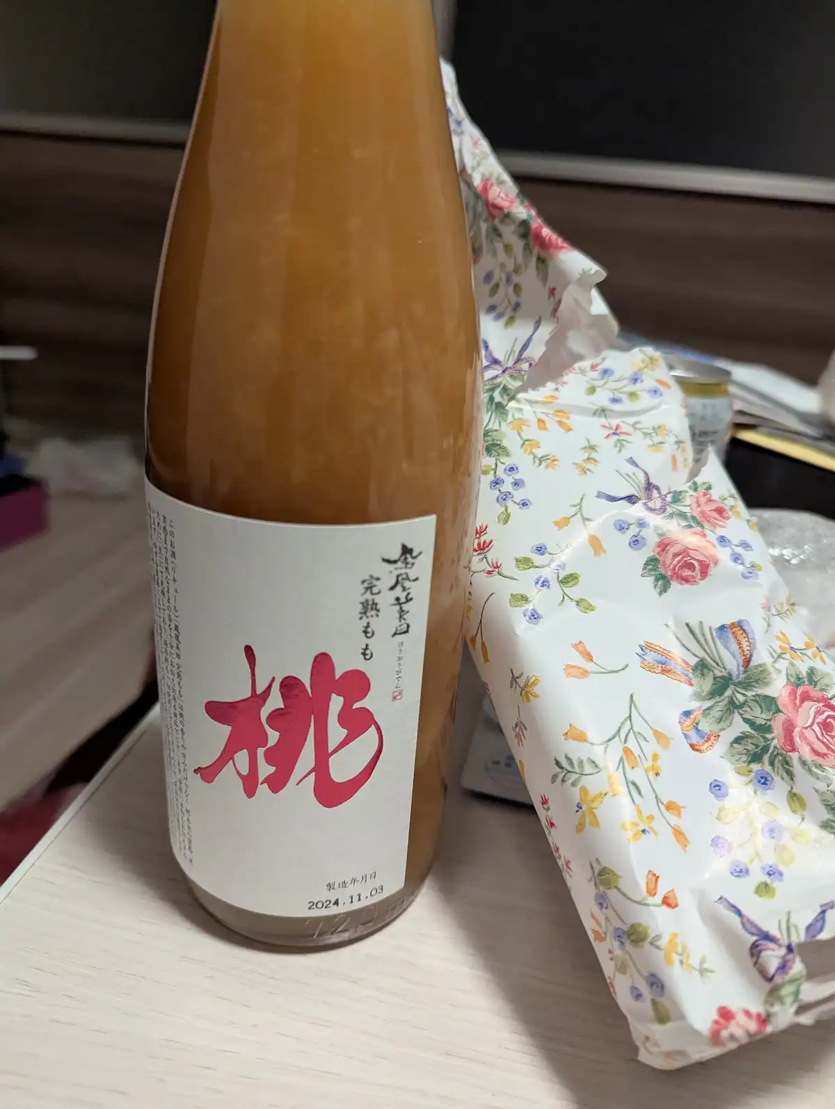 A bottle of Japanese peach-flavored sake with a white label featuring large red kanji '桃' (peach) and smaller text including…