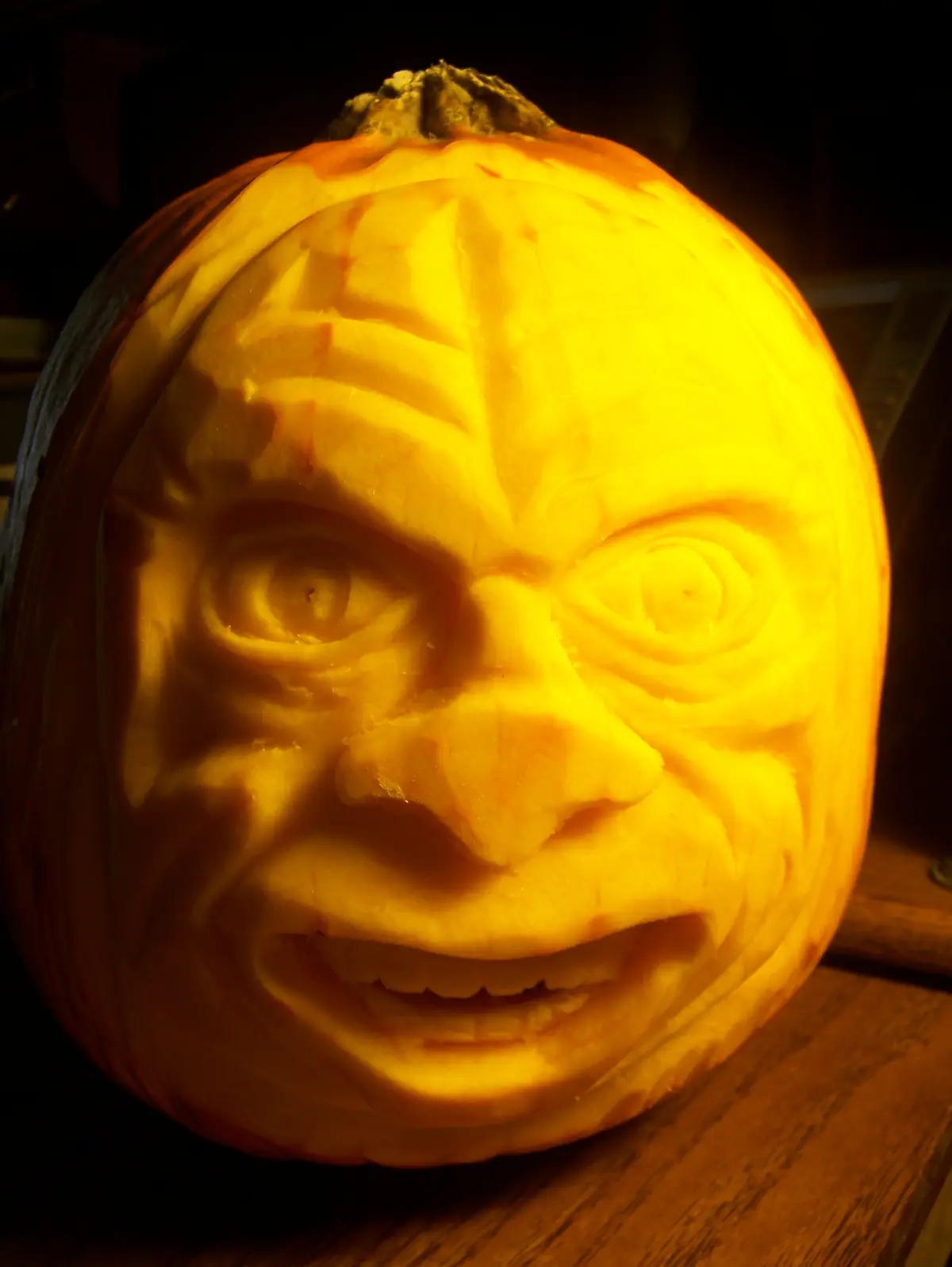 A close-up of a highly detailed, intricately carved pumpkin illuminated from within, revealing a realistic human-like face…