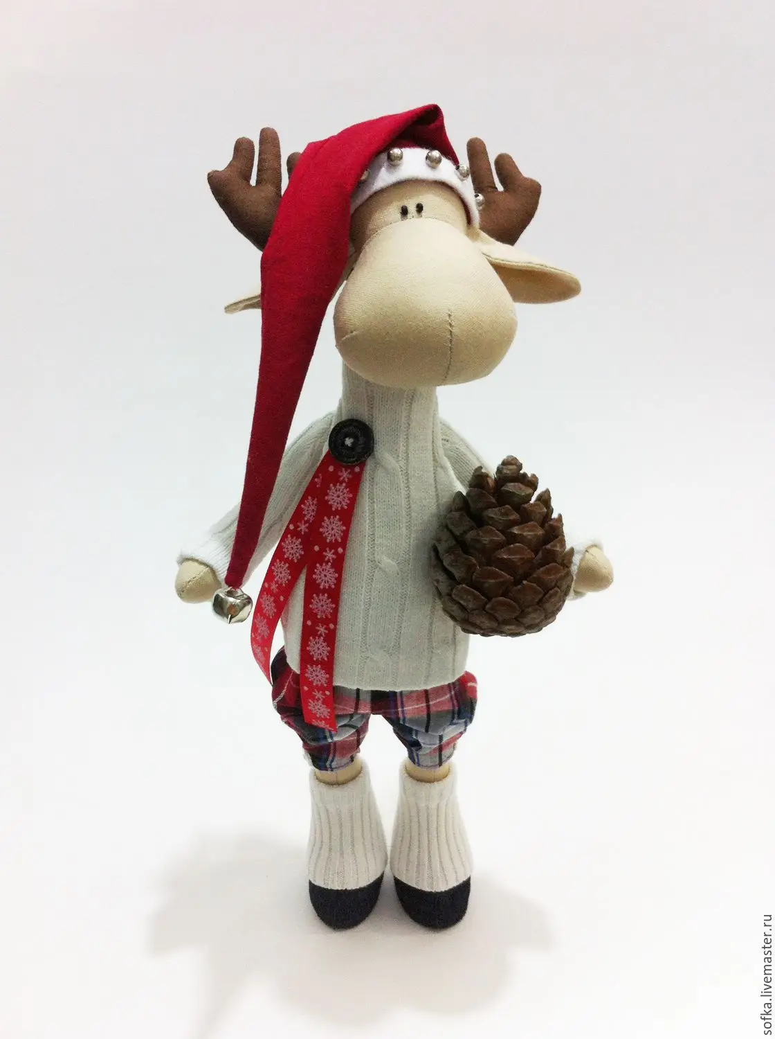 A handmade plush moose figurine dressed in festive winter attire including a red Santa hat with bells, a white sweater…