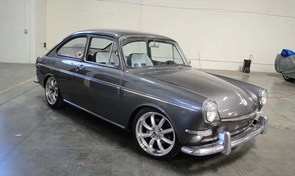 a silver 1963 volkswagen 1500 coupe is shown parked indoors on a concrete floor, featuring chrome bumpers, round headlights…