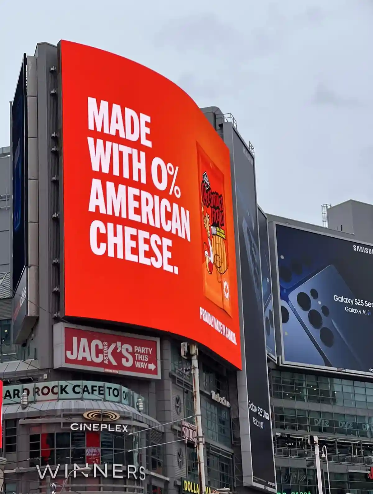 A large red billboard in a city displays the text 'MADE WITH 0% AMERICAN CHEESE.' alongside an image of a Cheez Whiz…