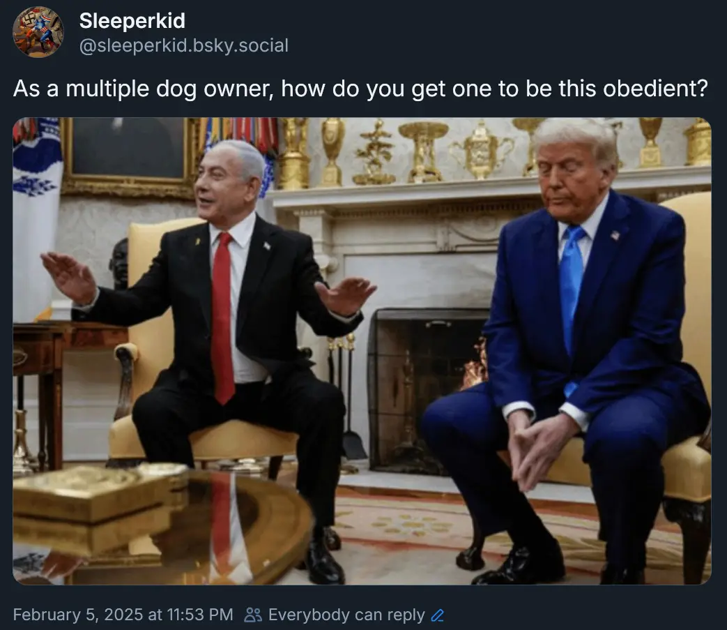 Two men in suits sit in ornate chairs in a formal room with a fireplace and golden trophies behind them. The man on the left…