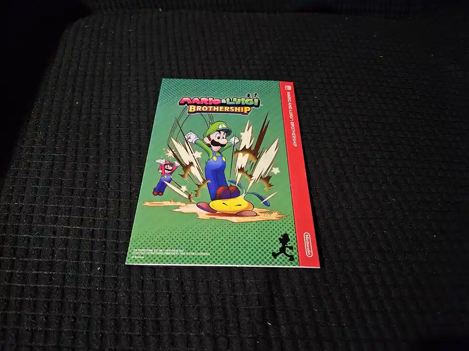 A promotional Nintendo Switch game case for 'Mario & Luigi: Brothership' rests on a dark textured surface. The cover art…