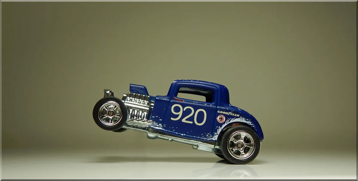 A blue Hot Wheels-style hot rod toy car with the number 920 on its side is photographed at a steep angle, appearing to be…