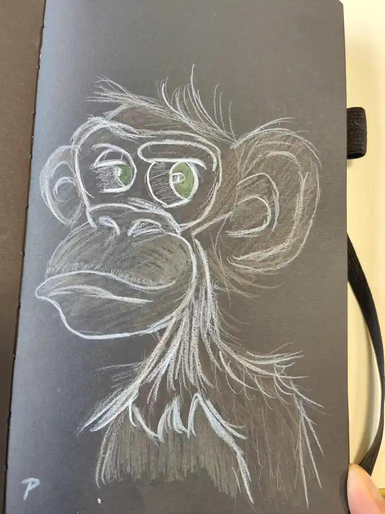 A chalk drawing on dark paper depicts a monkey with large, expressive green eyes and detailed fur, looking directly at the…
