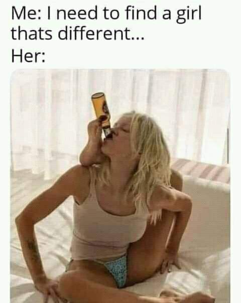 A blonde woman in a tank top and underwear sits on a bed, drinking directly from a beer bottle while looking upward. The…