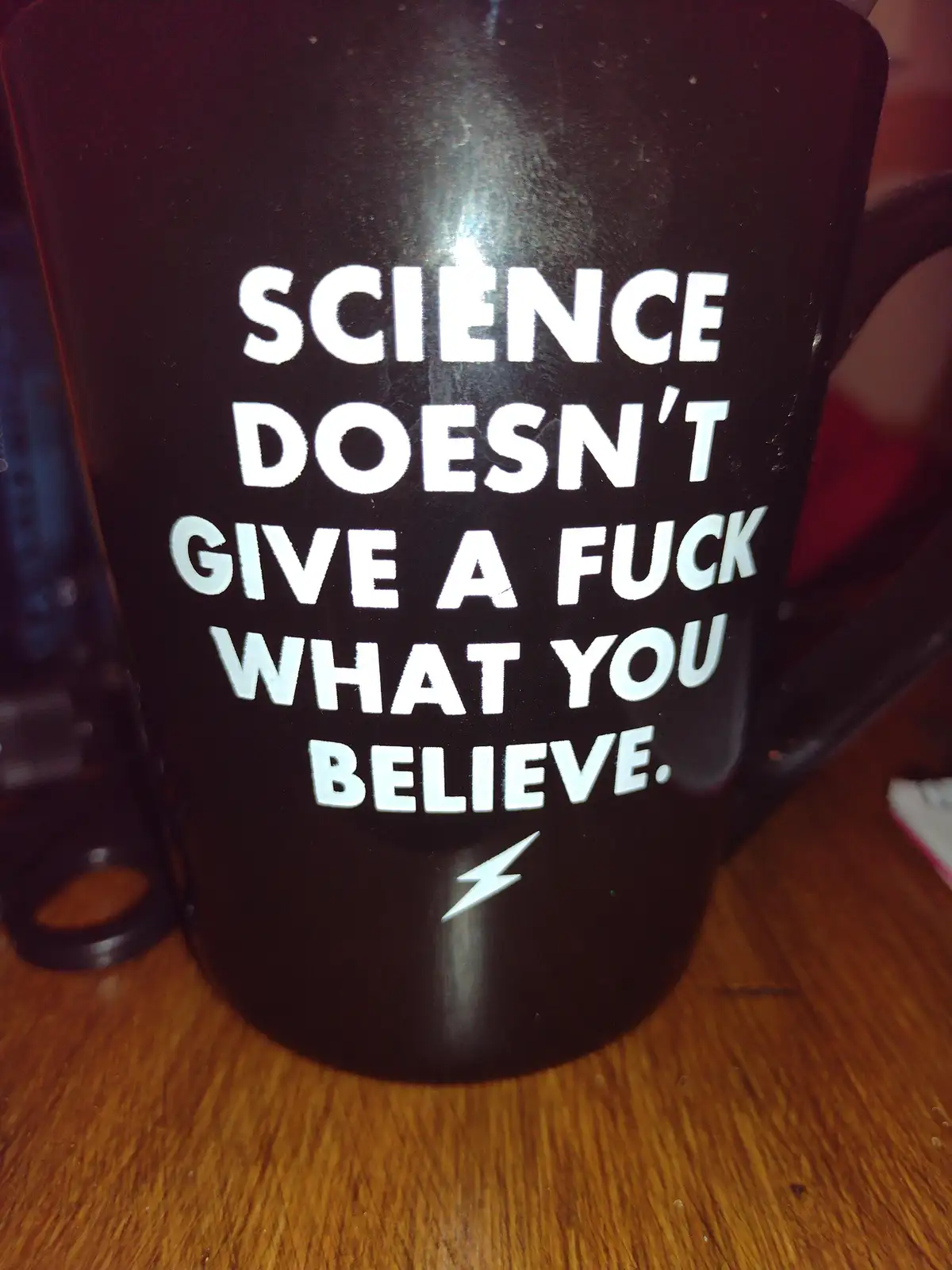 A close-up photo of a black mug sitting on a wooden surface, featuring bold white text that reads 'SCIENCE DOESN'T GIVE A…